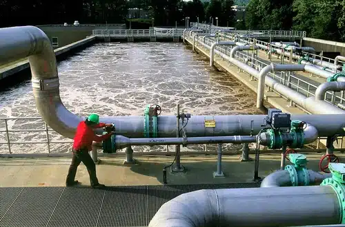 "Worker adjusting valves on a large pipeline at a wastewater treatment plant."