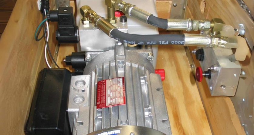 "Close-up view of an industrial pump system with connected hoses and electrical components, mounted on a wooden base."