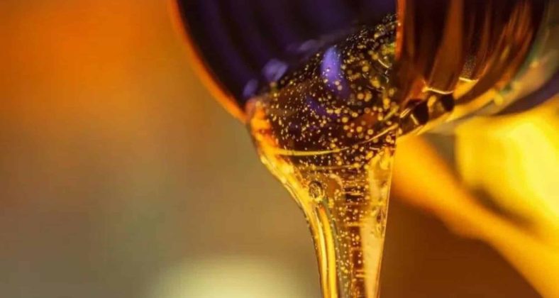 "Close-up of golden oil being poured from a container, with a rich, viscous texture and warm lighting in the background."